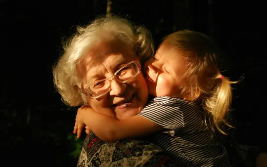 Een oma met bril en grijs haar krijgt een knuffel van haar kleindochter