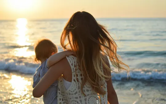 Een moeder draagt haar kind op het strand bij zonsondergang